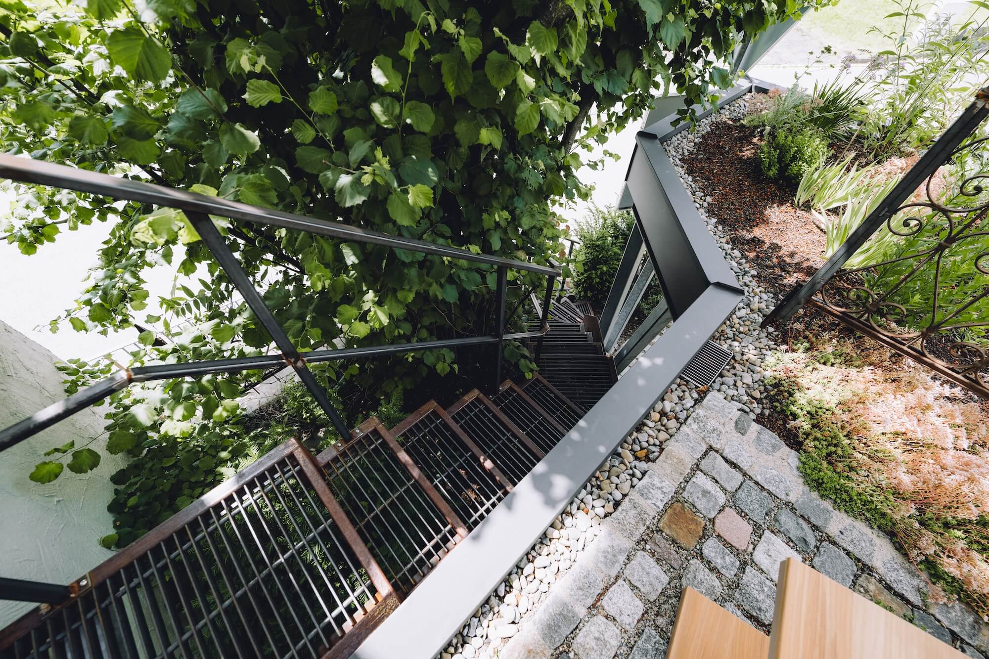 Kleiner Dachgarten mit Treppe, Naturstein und üppiger Bepflanzung Ein farbenfroher Sonnenschirm schützt den Gartentisch auf der gepflasterten Terrasse zwischen Natursteinmauern und üppigem Grün von Hübner.
