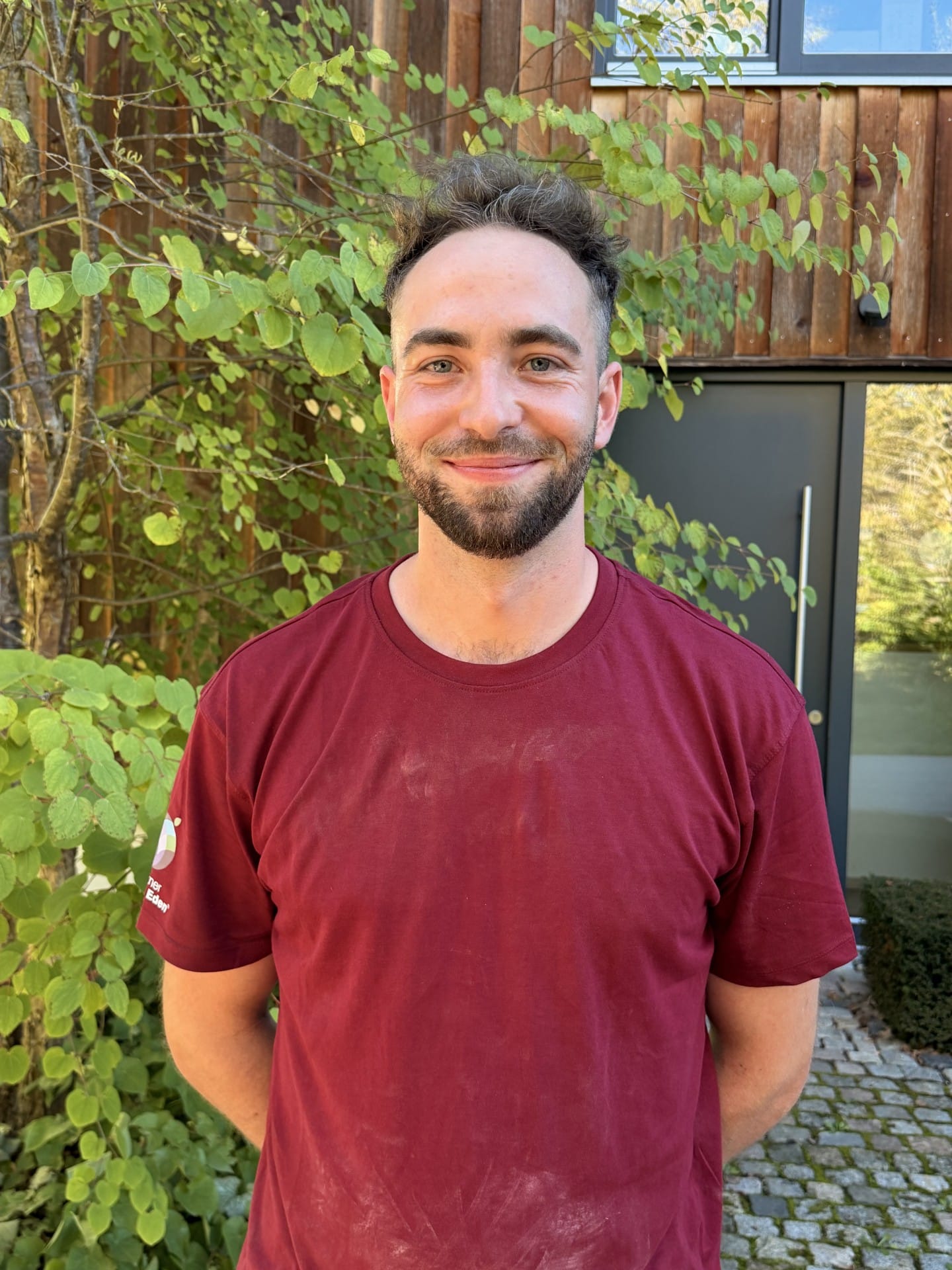 Elias Karlström Junger Mann mit braunen Haaren trägt eine schwarze Weste und steht im Garten.